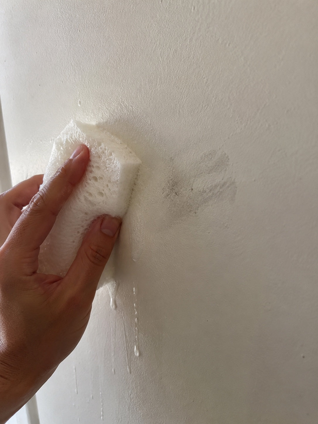 Une eponge humide efface a moitie une trace grise sur un mur peint